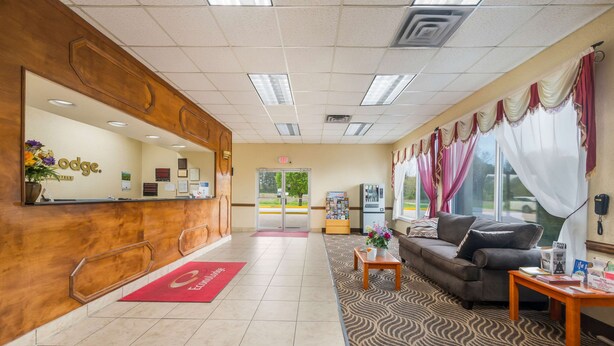 A hotel reception area with a wooden reception desk, a red carpet, a sofa, and a patterned carpet. - Econo Lodge Cullman South (Cullman)