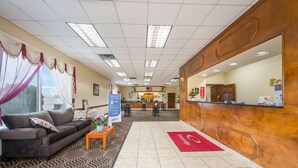 A reception area with a wooden reception desk, a waiting area with a sofa and coffee table, and a patterned carpet. - Econo Lodge Cullman South (Cullman)