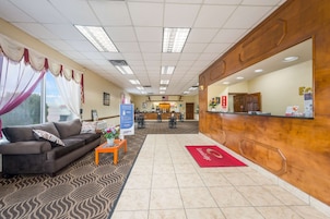 Una zona de recepción con un mostrador de madera, un área de espera con sofá y mesa de centro, y una alfombra estampada.