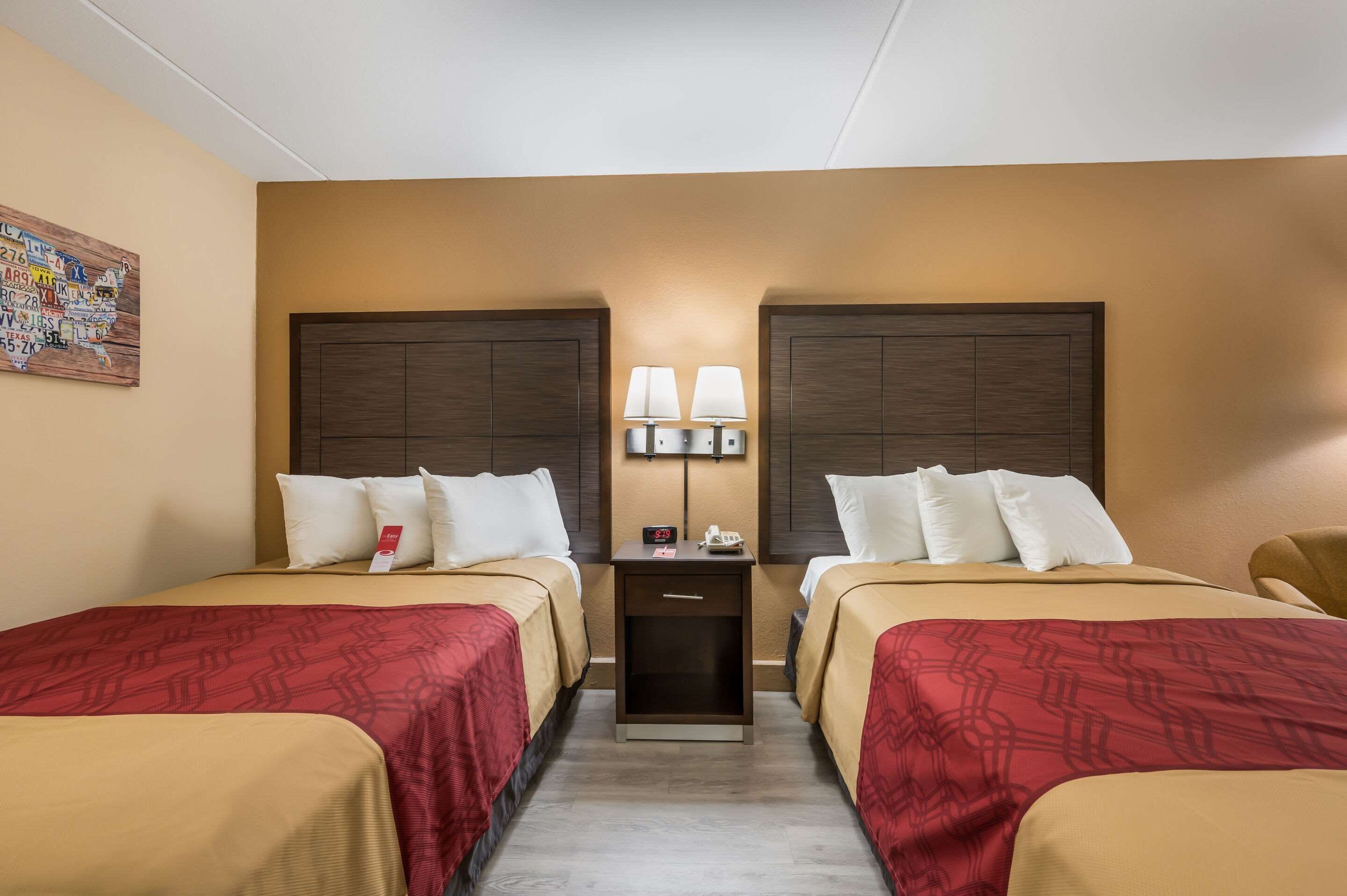 A hotel room with two beds, a nightstand with lamps, and a wall clock.