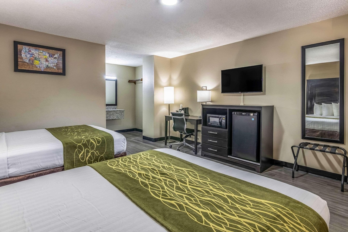 A hotel room with two beds, a desk, a television, and a mirror.