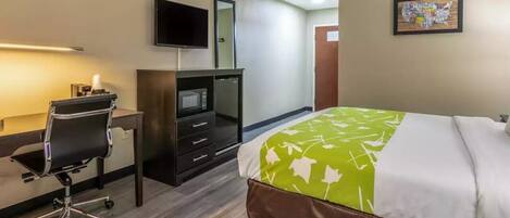 Habitación de hotel con cama, escritorio con silla, televisor, espejo y un cuadro en la pared.