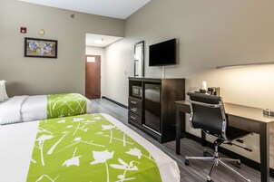 Habitación de hotel con dos camas, un escritorio, una silla, un televisor, un aparador y un detector de incendios.