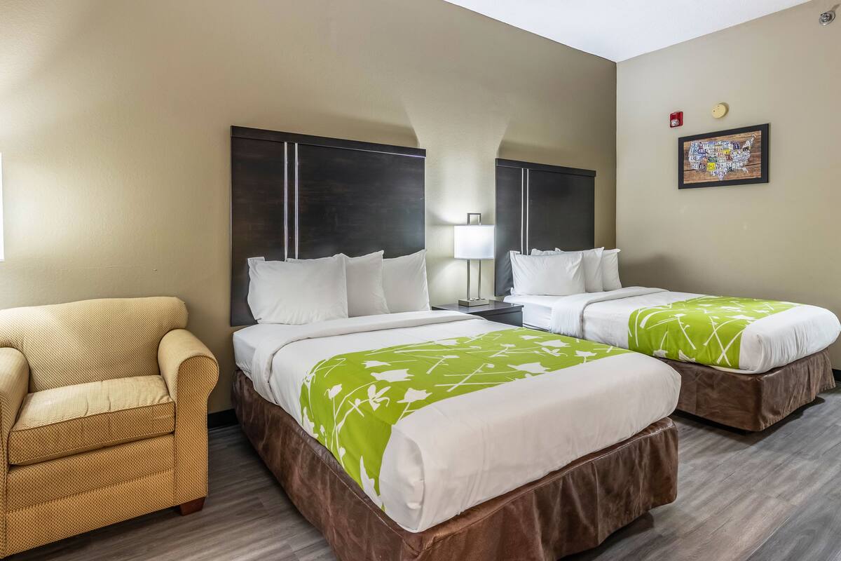 A hotel room with two beds, a sofa, a nightstand, a lamp, and a wall-mounted map.