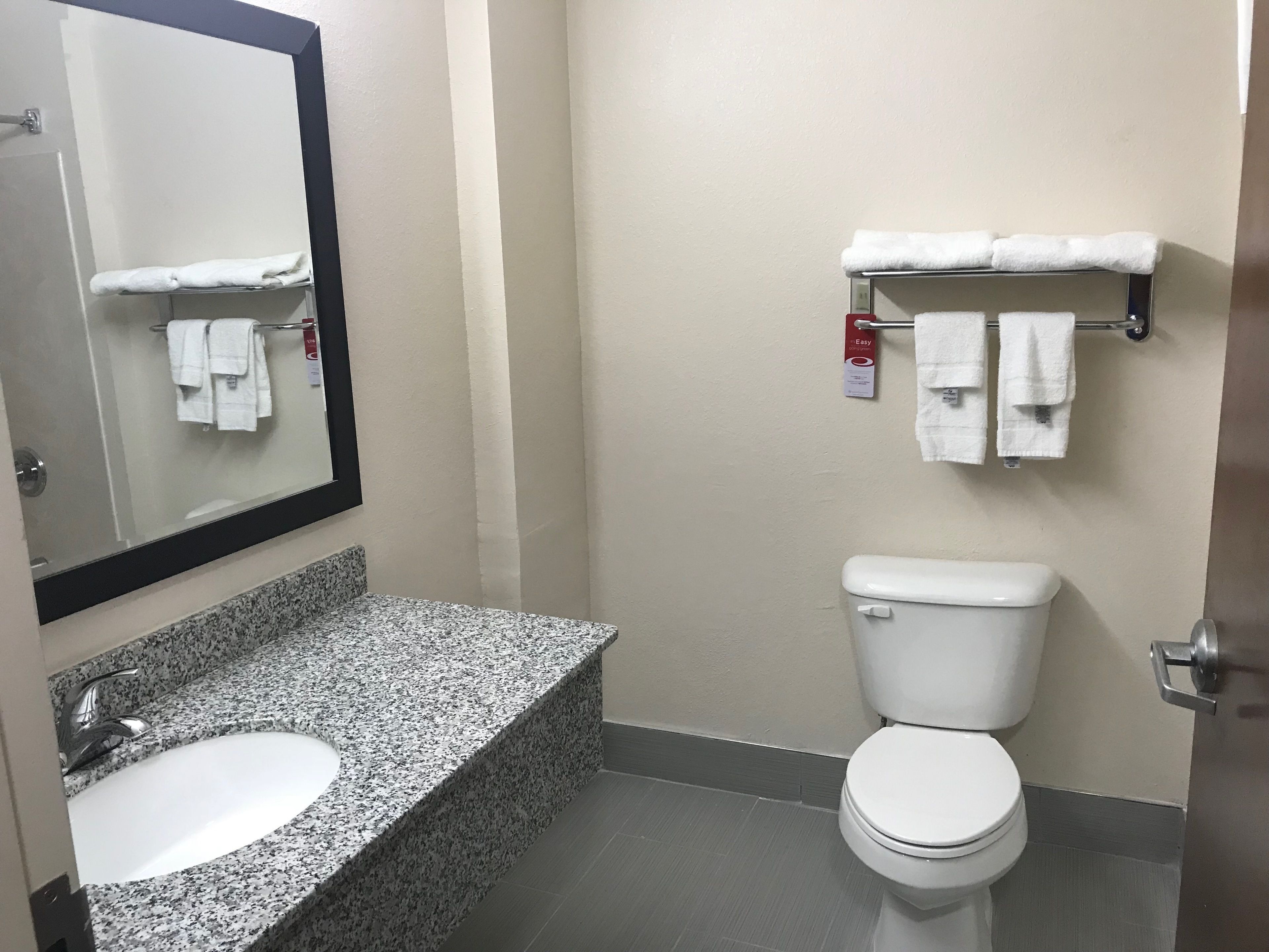 Un baño con lavamanos de encimera de granito, inodoro blanco y toallero con toallas.