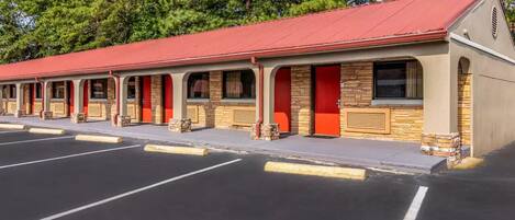 Una hilera de habitaciones de motel con puertas y techo rojos, con árboles de fondo.