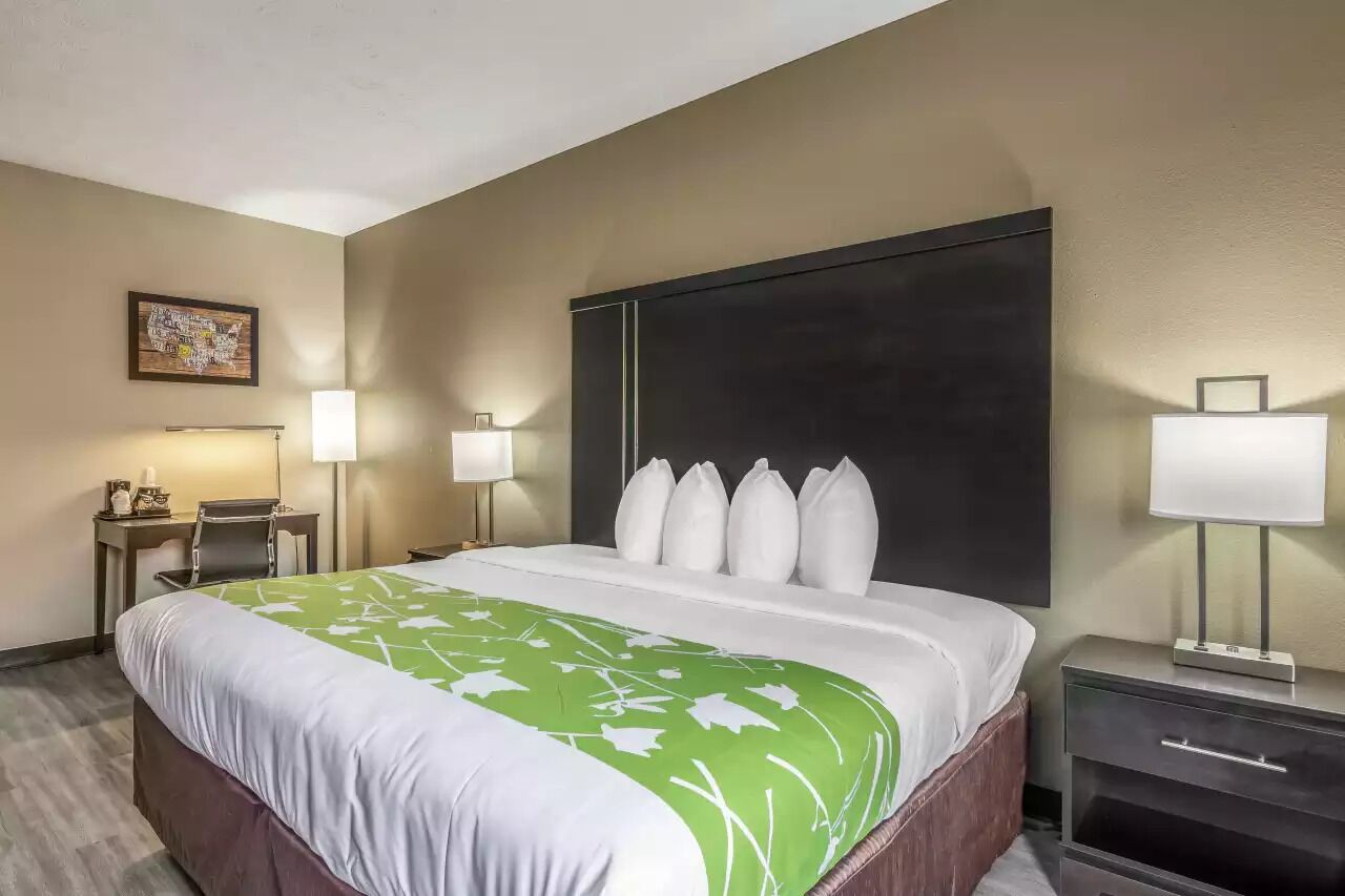 A hotel room with a large bed, two bedside tables with lamps, a desk with a chair, and a framed picture on the wall.