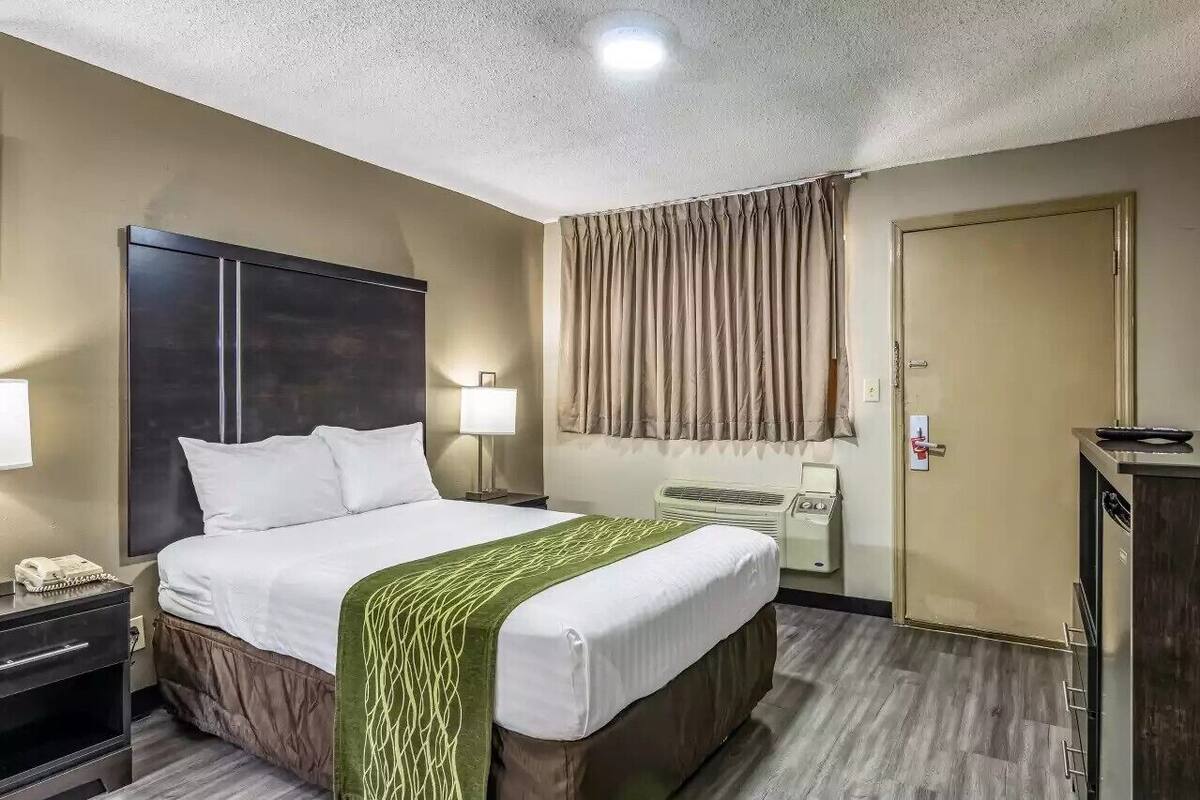 A hotel room with a large bed, bedside lamps, a wardrobe, a desk with a telephone, and a door with a lock.