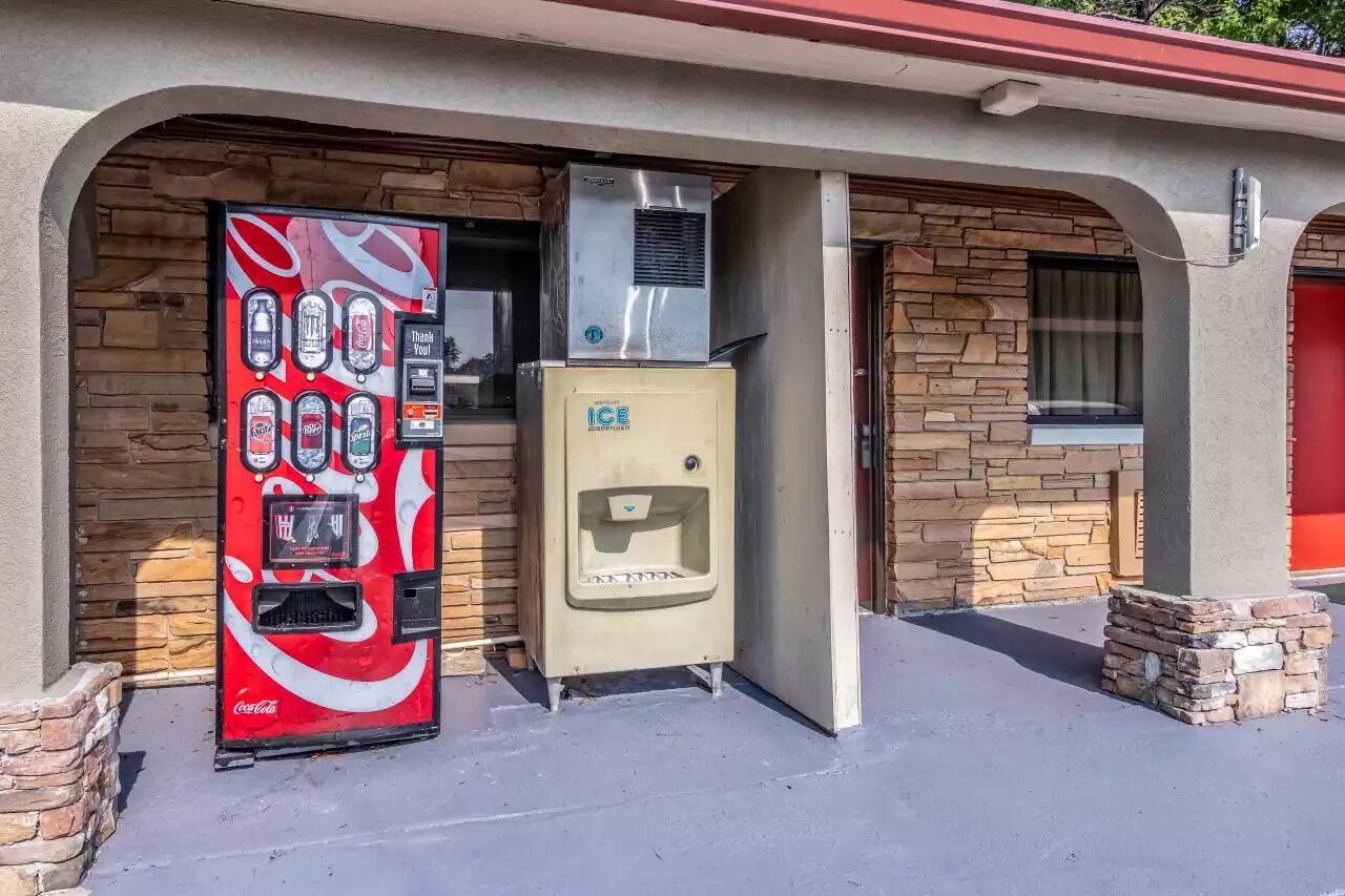 Un distributeur automatique de Coca-Cola et un distributeur de glaçons se trouvent à l’extérieur d’un bâtiment aux murs en pierre et à la porte rouge.