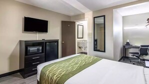 Una camera d'albergo con un letto, una scrivania, una sedia, un televisore e un frigobar.