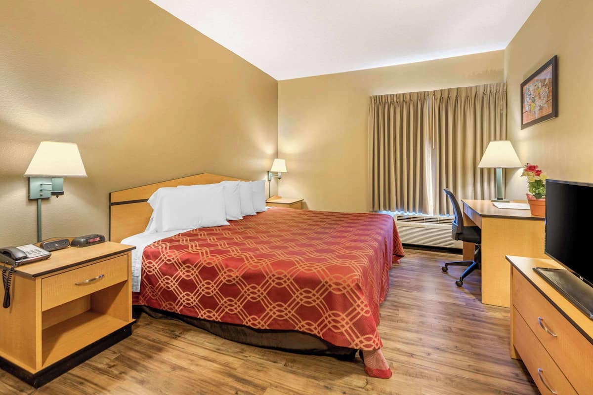 A hotel room with a bed, bedside tables, lamps, a desk with a chair, a television, and a window with curtains.