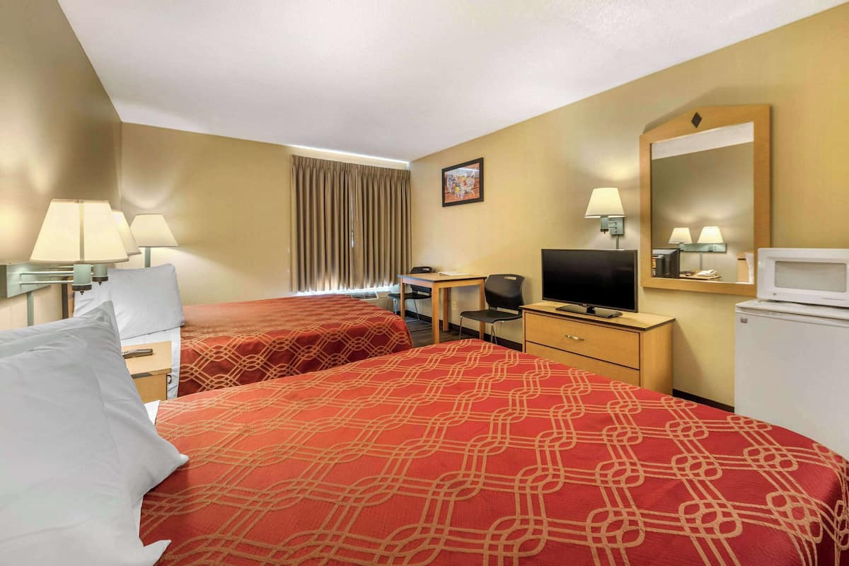 A hotel room with two beds, a desk, a television, a mirror, and a refrigerator.