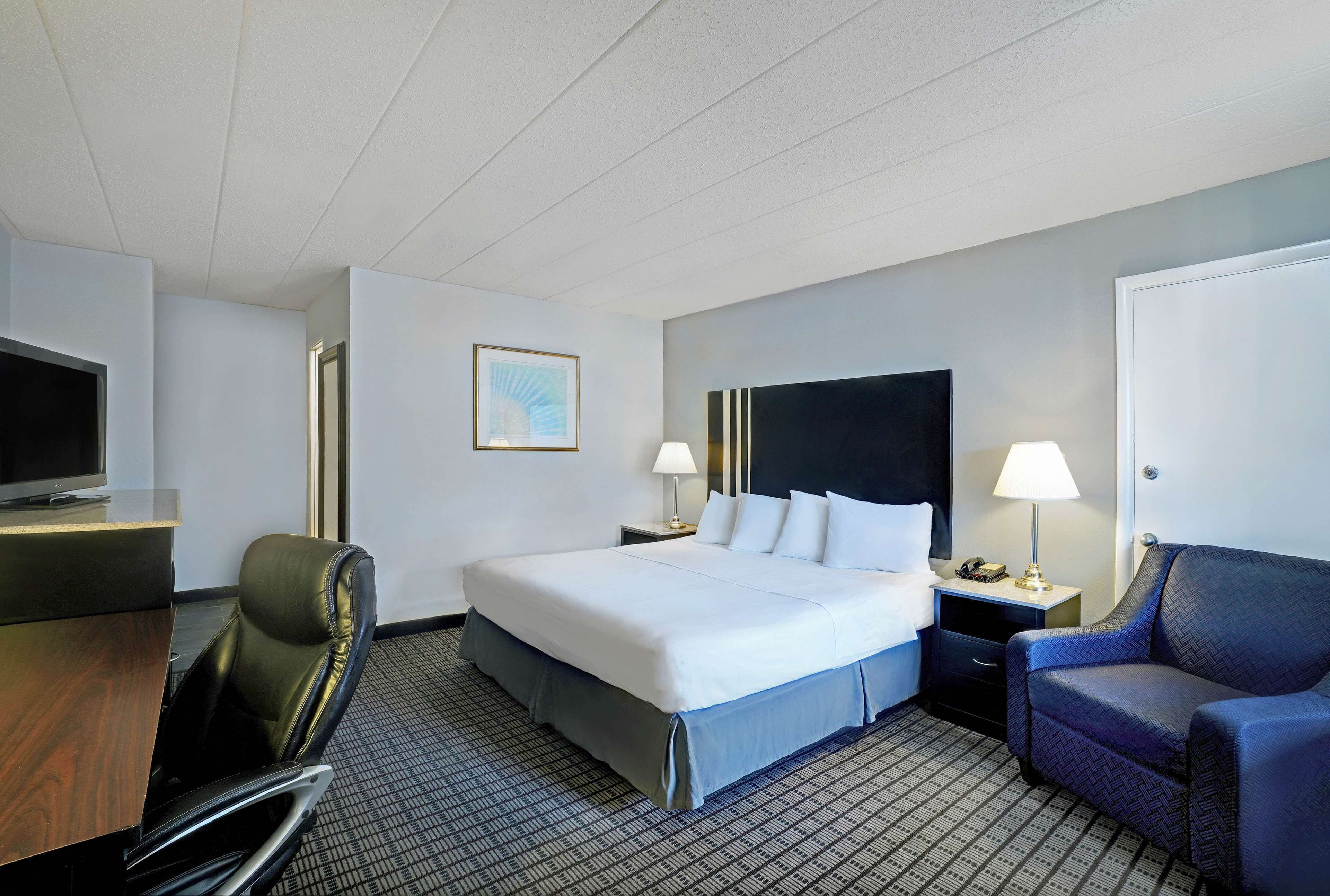 A hotel room with a bed, a desk, a chair, a TV, and a lamp.