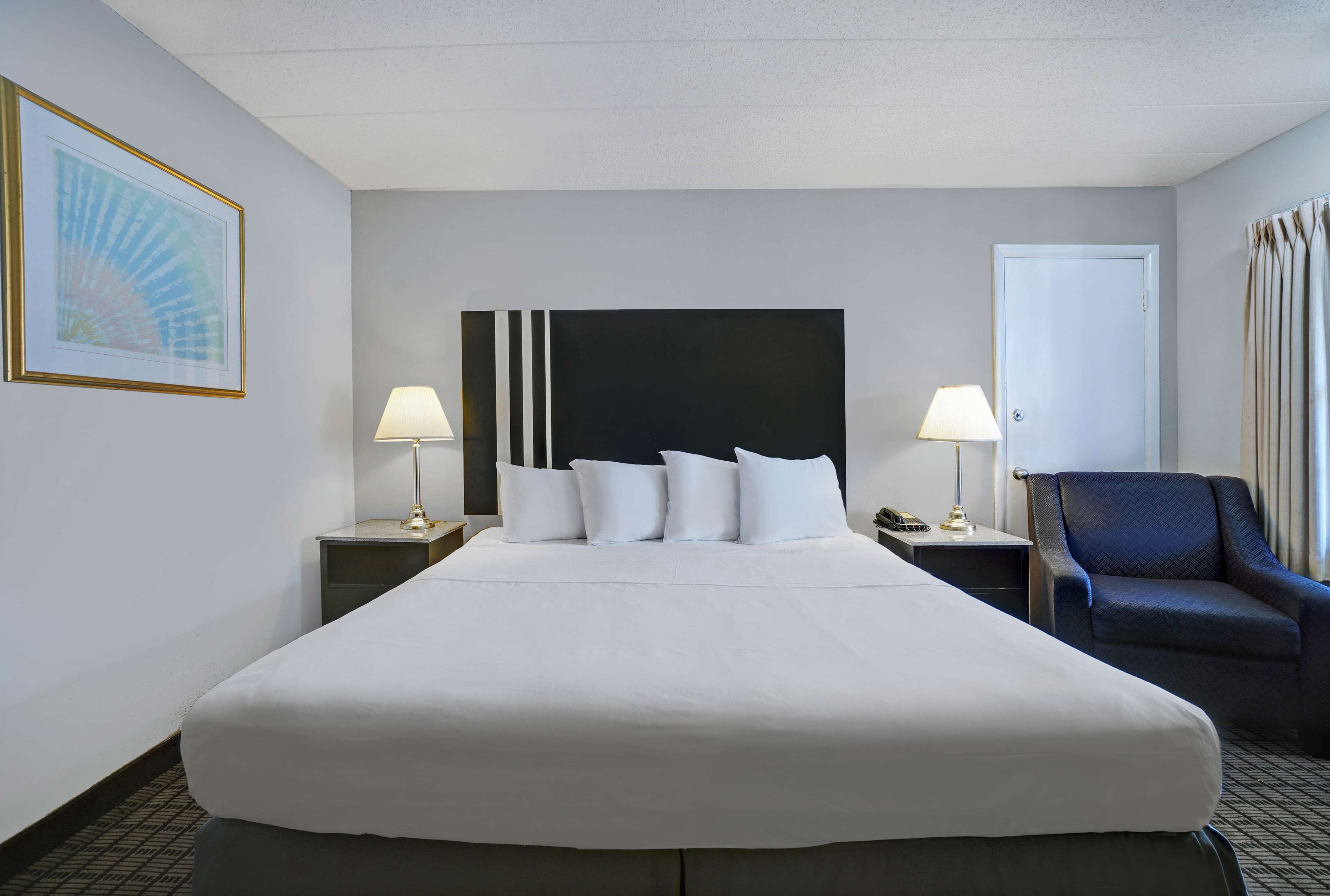 Habitación de hotel con una cama grande, dos mesitas de noche con lámparas, una silla y una puerta.