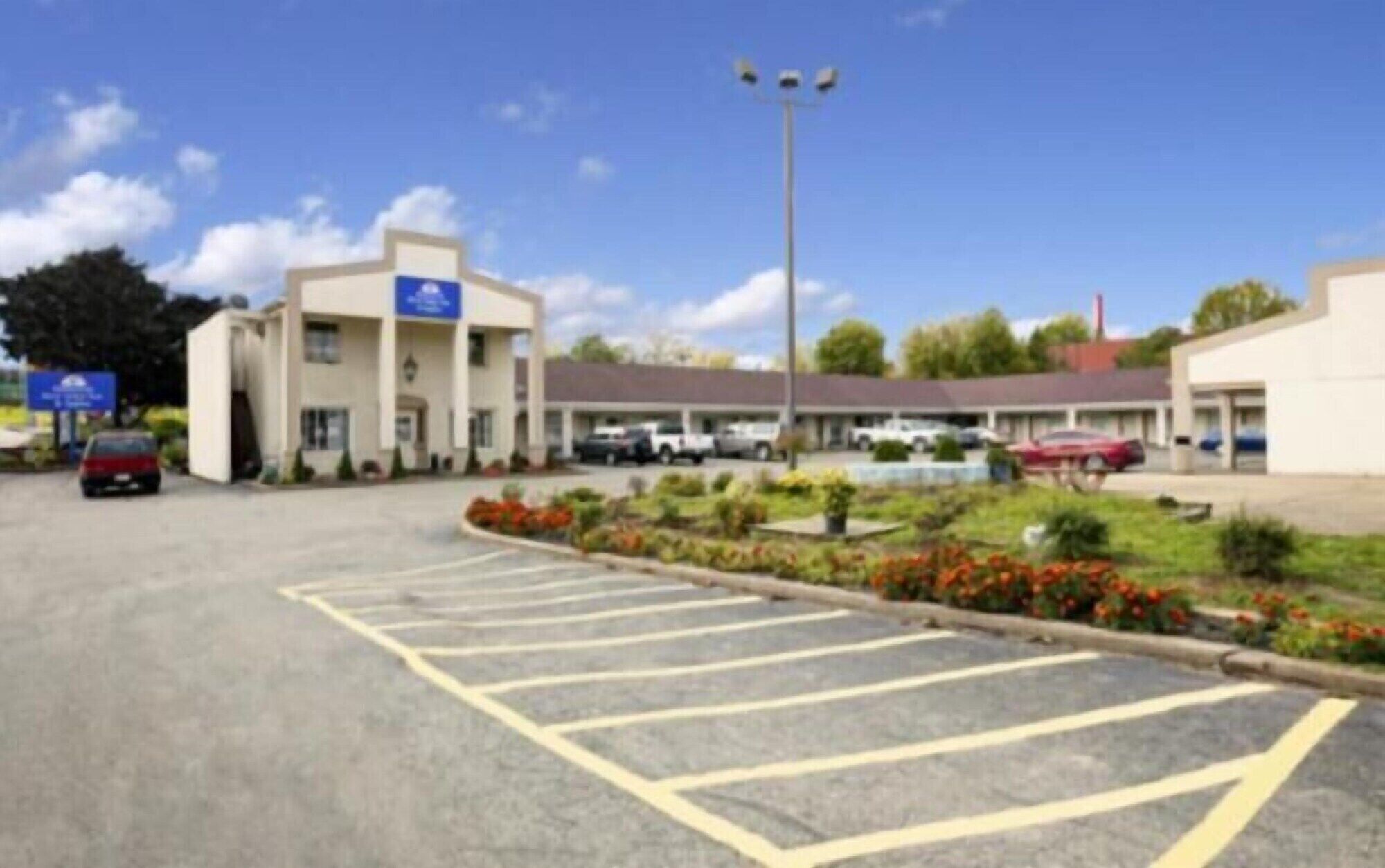 Un parking avec des places délimitées, un bâtiment avec une enseigne bleue et un espace paysager agrémenté de fleurs.