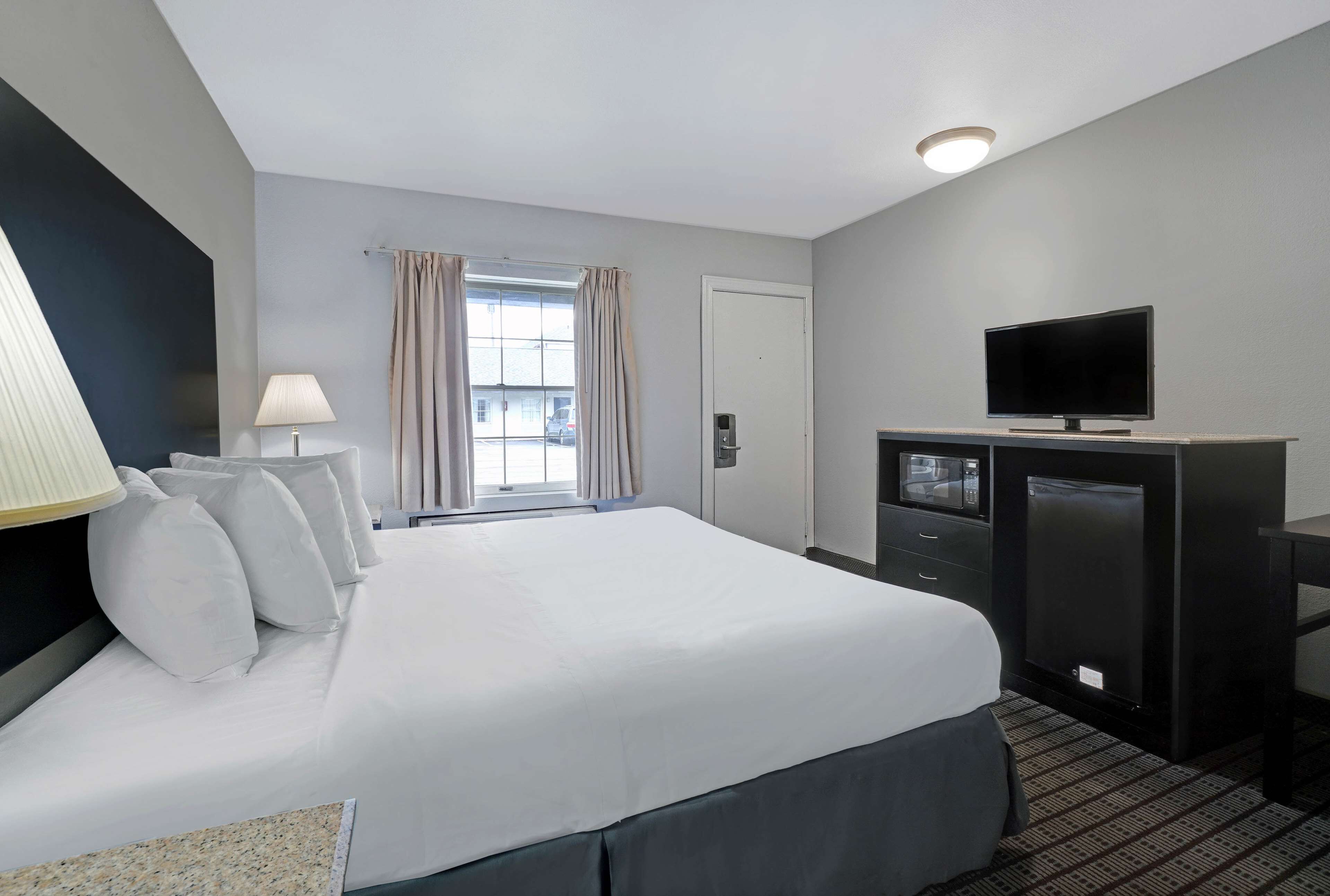 Una habitación de hotel con una cama grande, televisión, escritorio y ventana con cortinas.