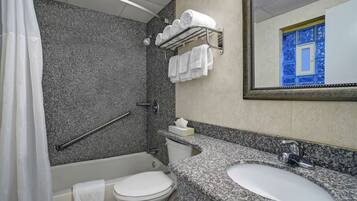Een badkamer met een wastafel met een granieten blad, een wit toilet, een douche met glazen deur en een handdoekhouder met opgevouwen handdoeken.