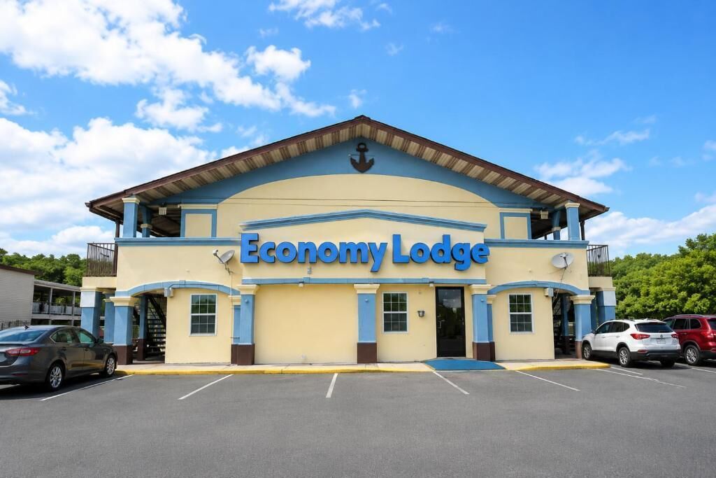 Ein zweistöckiges Economy Lodge mit flachem Dach, einer Satellitenschüssel und einem Parkplatz mit mehreren Autos.