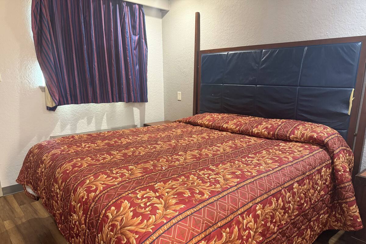 Une chambre d’hôtel avec un grand lit, une tête de lit et une fenêtre avec des rideaux.