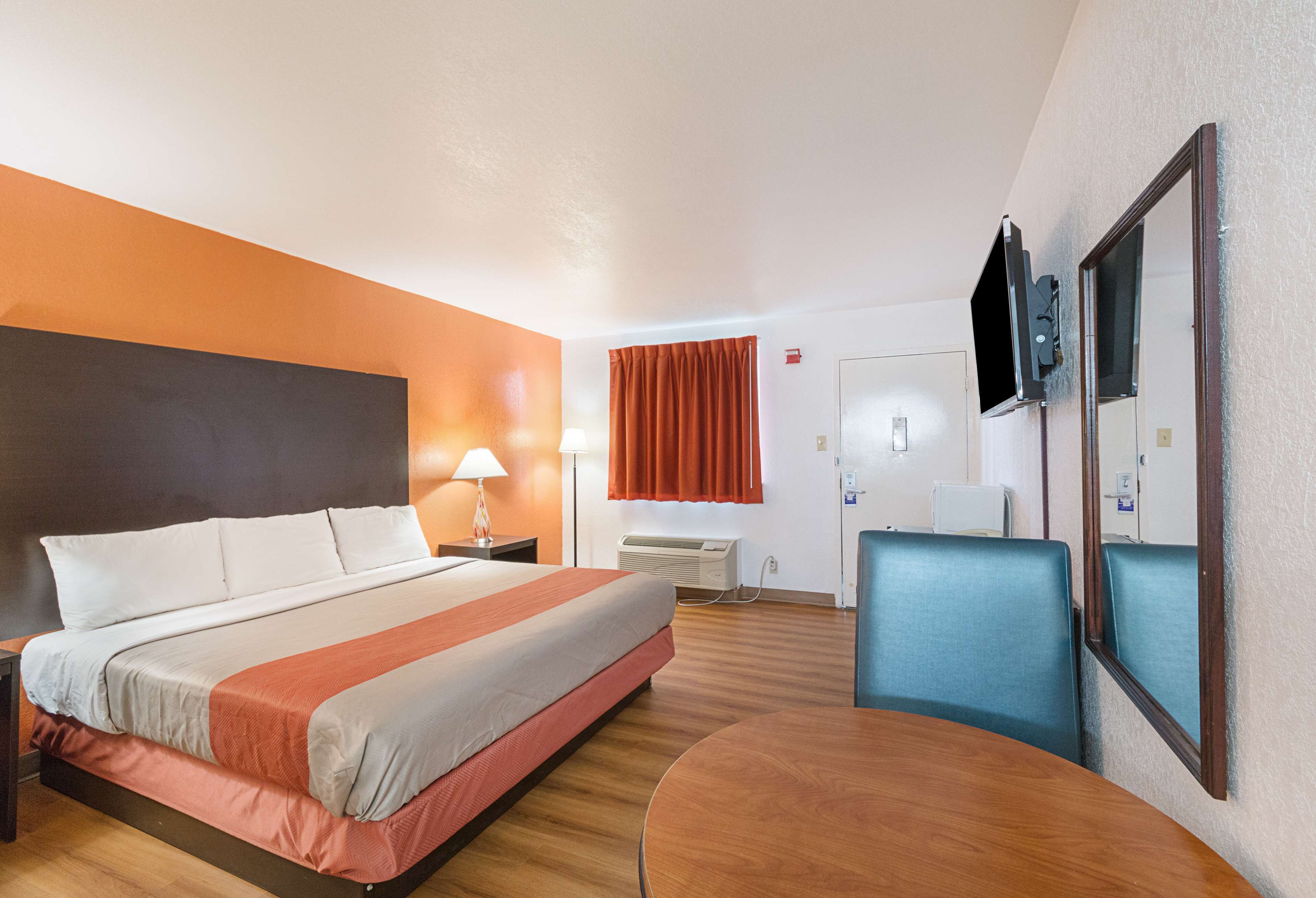 Een hotelkamer met een bed, bureau, stoel, televisie en airconditioning.