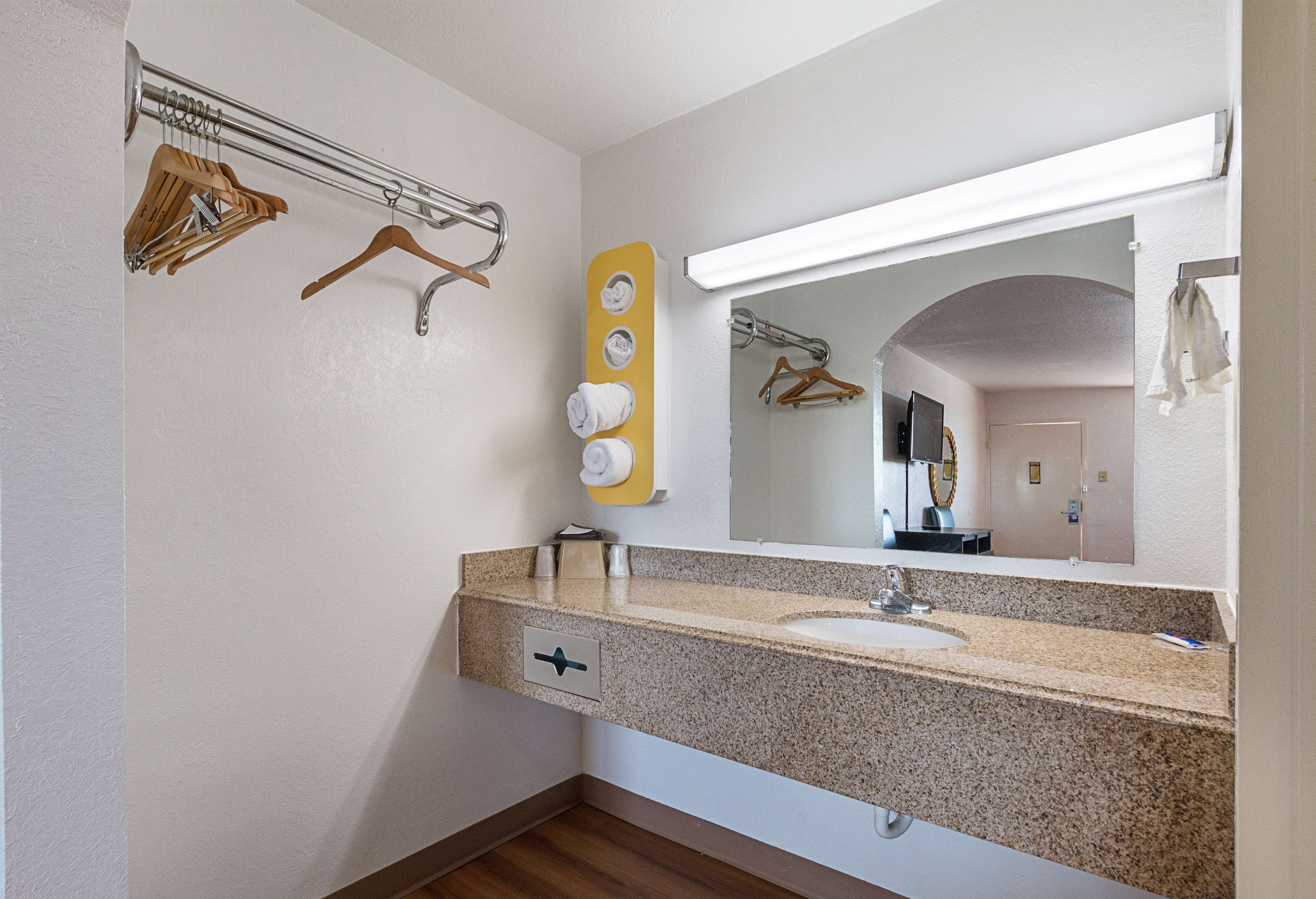 A bathroom with a granite countertop sink, a mirror, a towel rack, and a towel dispenser.