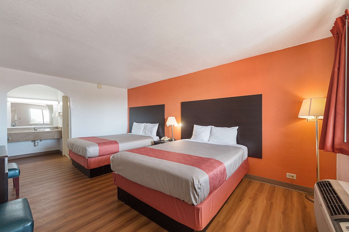 A hotel room with two beds, a desk, a mirror, and a bathroom.