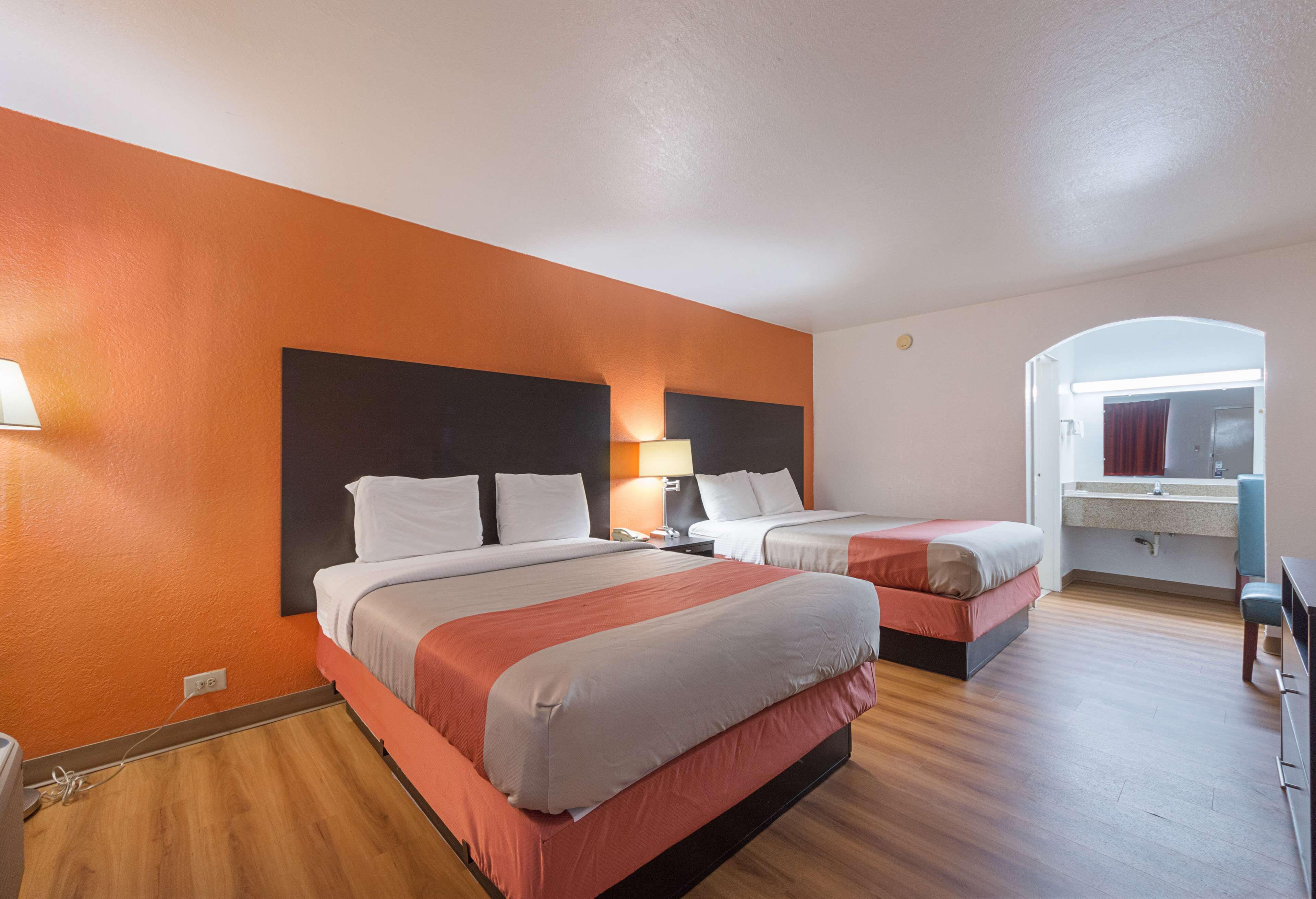 Ein Hotelzimmer mit zwei Betten, einem Badezimmer mit Spiegel und Holzboden.