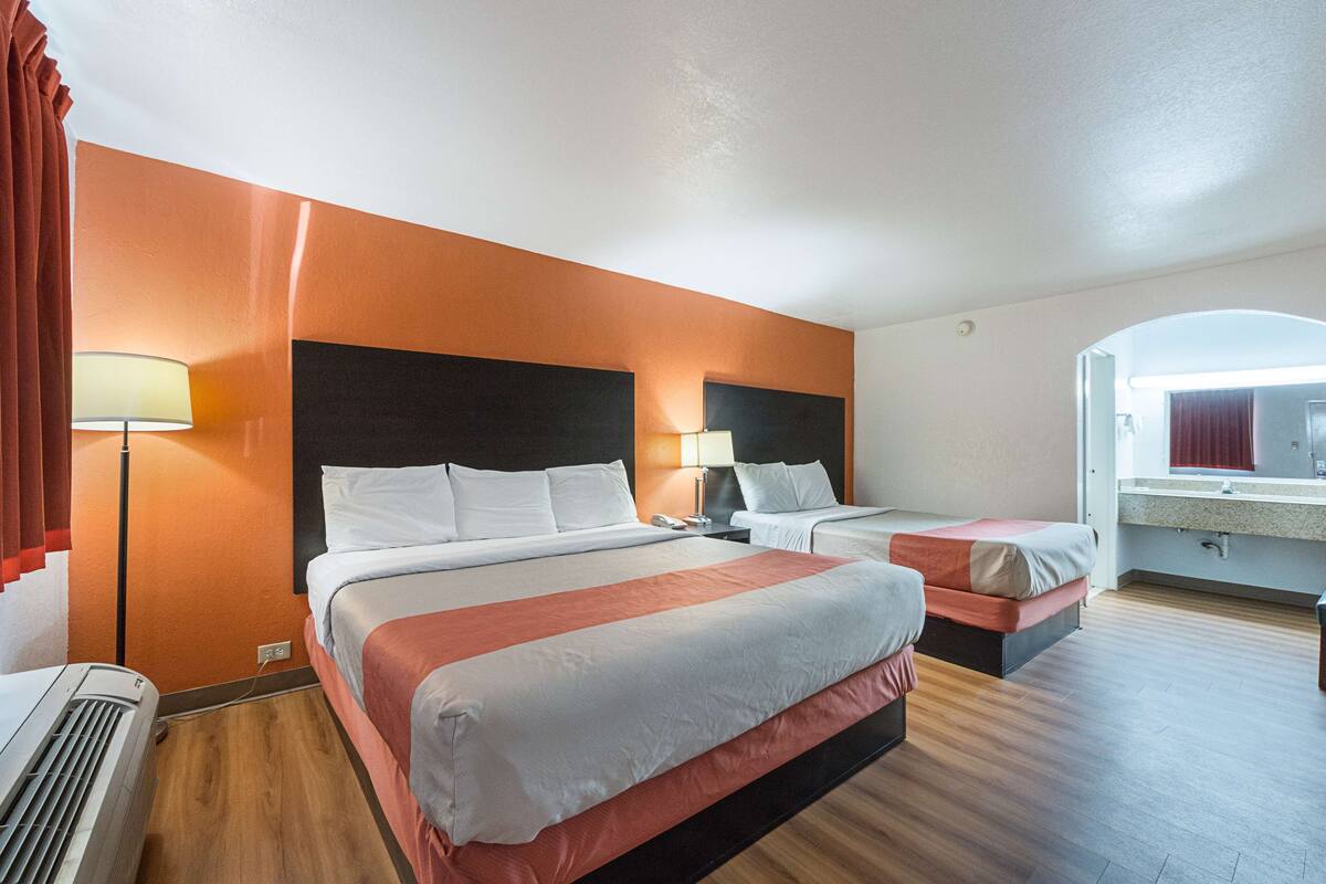 A hotel room with two beds, a large window, a bathroom with a mirror, and a heater.
