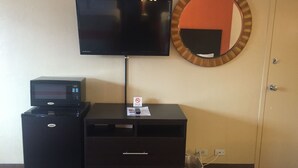 Habitación con televisor de pantalla plana en la pared, una pequeña impresora sobre un mueble, un cubo de basura y una puerta.