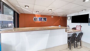 Un área de recepción con mostrador, sillas, un reloj y una televisión.