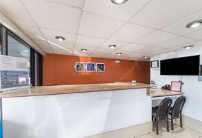 Un área de recepción con mostrador, sillas, un reloj y una televisión.