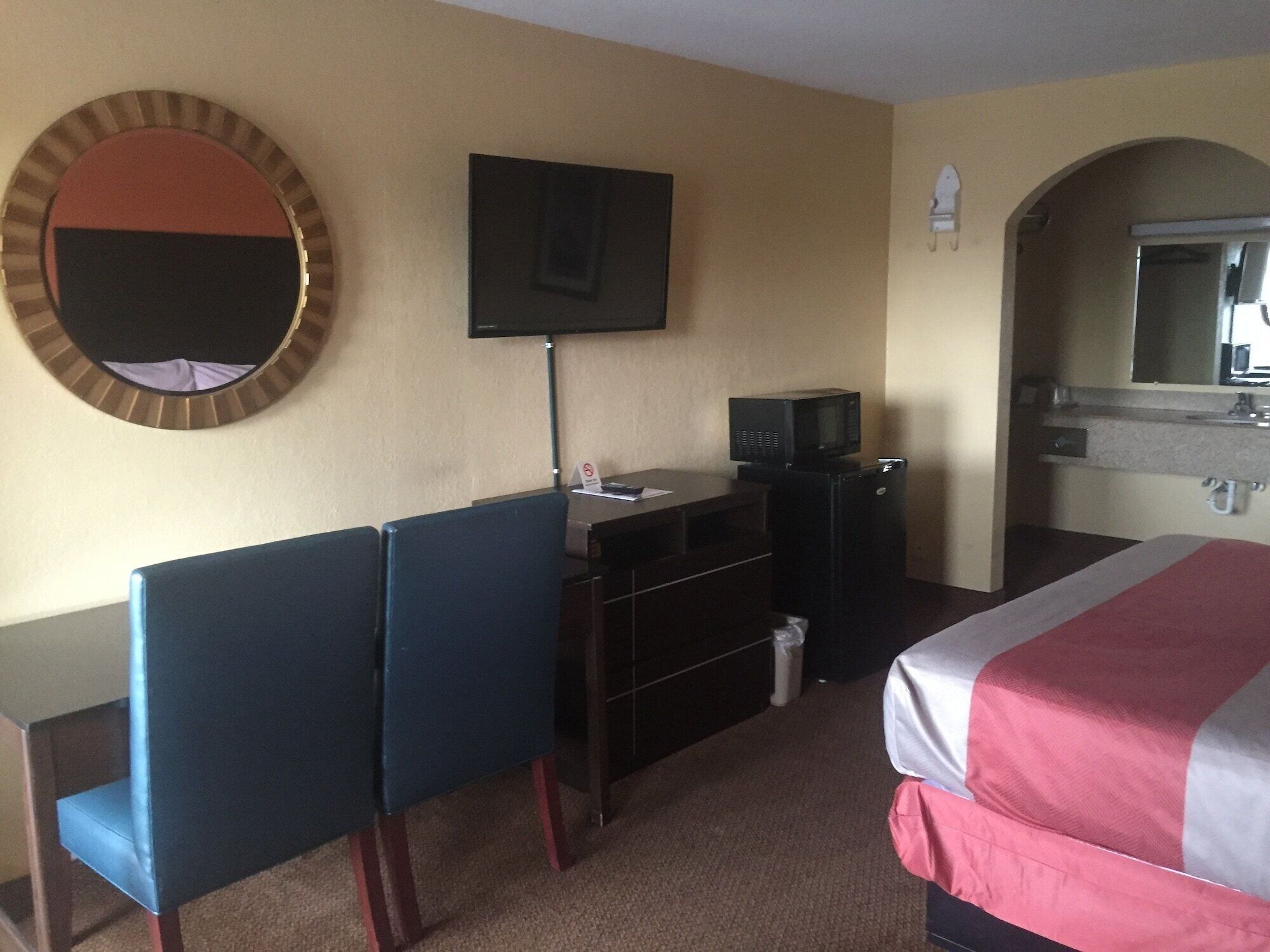 Une chambre d’hôtel comprenant un lit, un bureau avec une chaise, une télévision, un four à micro-ondes et une salle de bain avec un miroir.