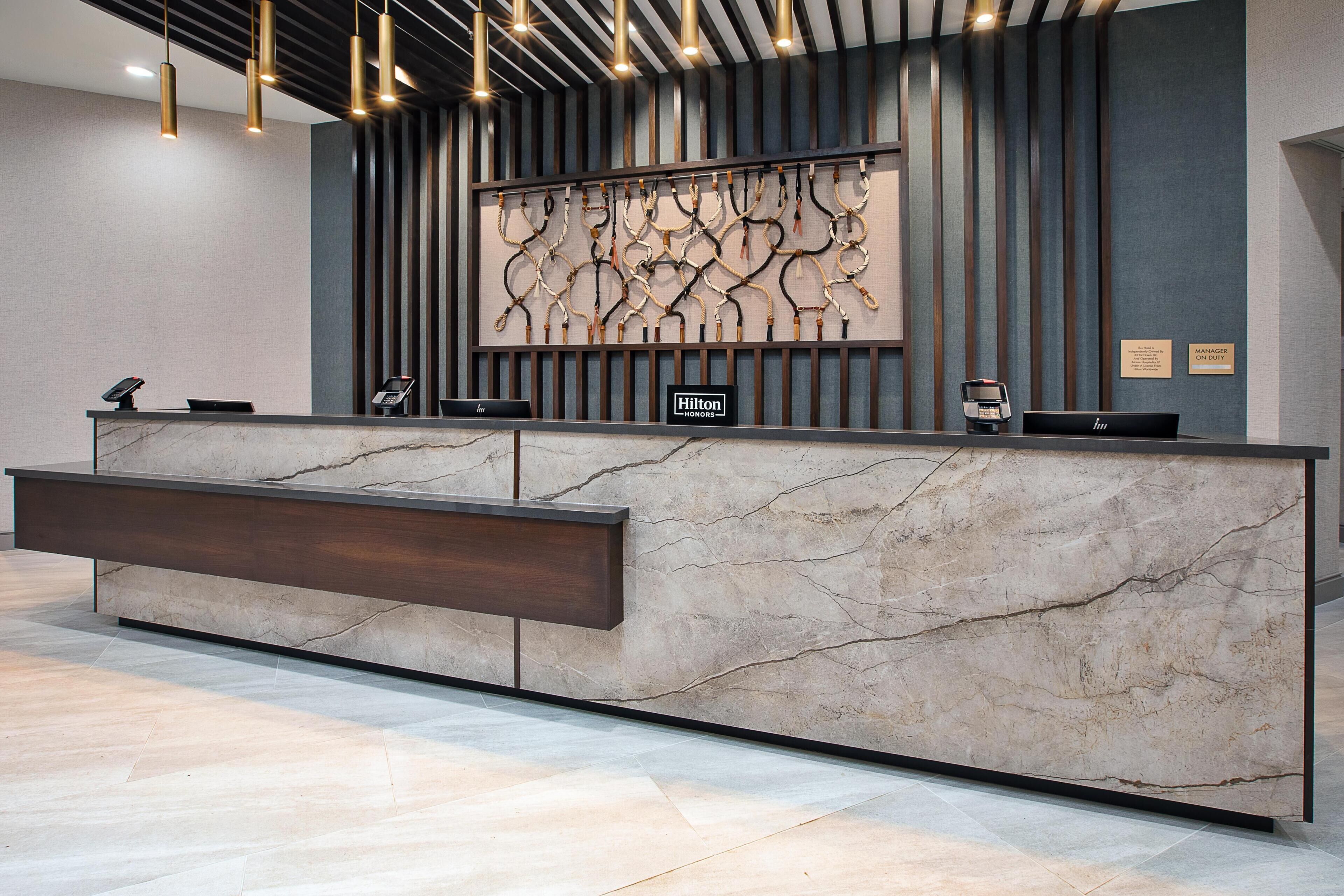 A hotel reception desk with a marble counter, a modern light fixture, and a wall-mounted artwork.