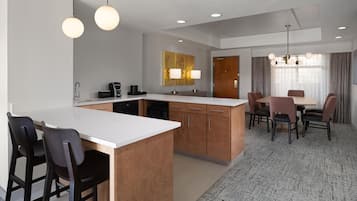 A modern hotel room with a kitchenette, dining area, and a large window with curtains.