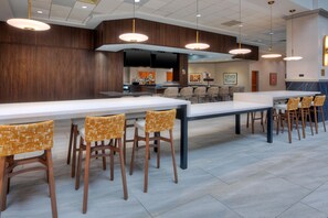 A modern bar area with long tables and chairs, a television screen, and a bar counter with various bottles. - Embassy Suites by Hilton Franklin Cool Springs (Franklin)