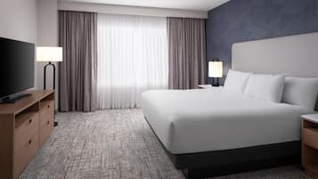 A hotel room with a large bed, a flat-screen TV, a desk, and a lamp.