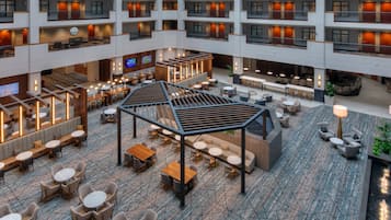 Vestíbulo de hotel de varios niveles con un espacio central abierto, zonas de estar y un bar.