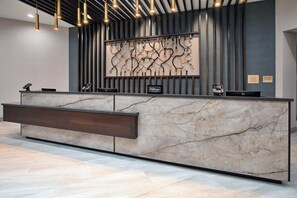 Un mostrador de recepción de hotel con encimera de mármol, una lámpara moderna y una obra de arte colgada en la pared.