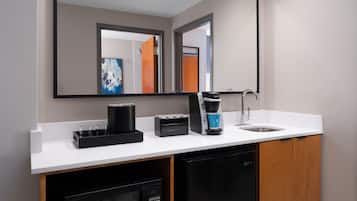 A modern bathroom with a white countertop, a coffee maker, a sink, and a mirror.