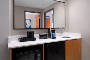 Un baño moderno con un mostrador blanco, una cafetera, un lavabo y un espejo.