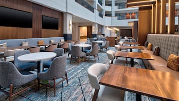 A hotel lobby with multiple seating areas, including round tables and sofas, and a high ceiling with a modern design.