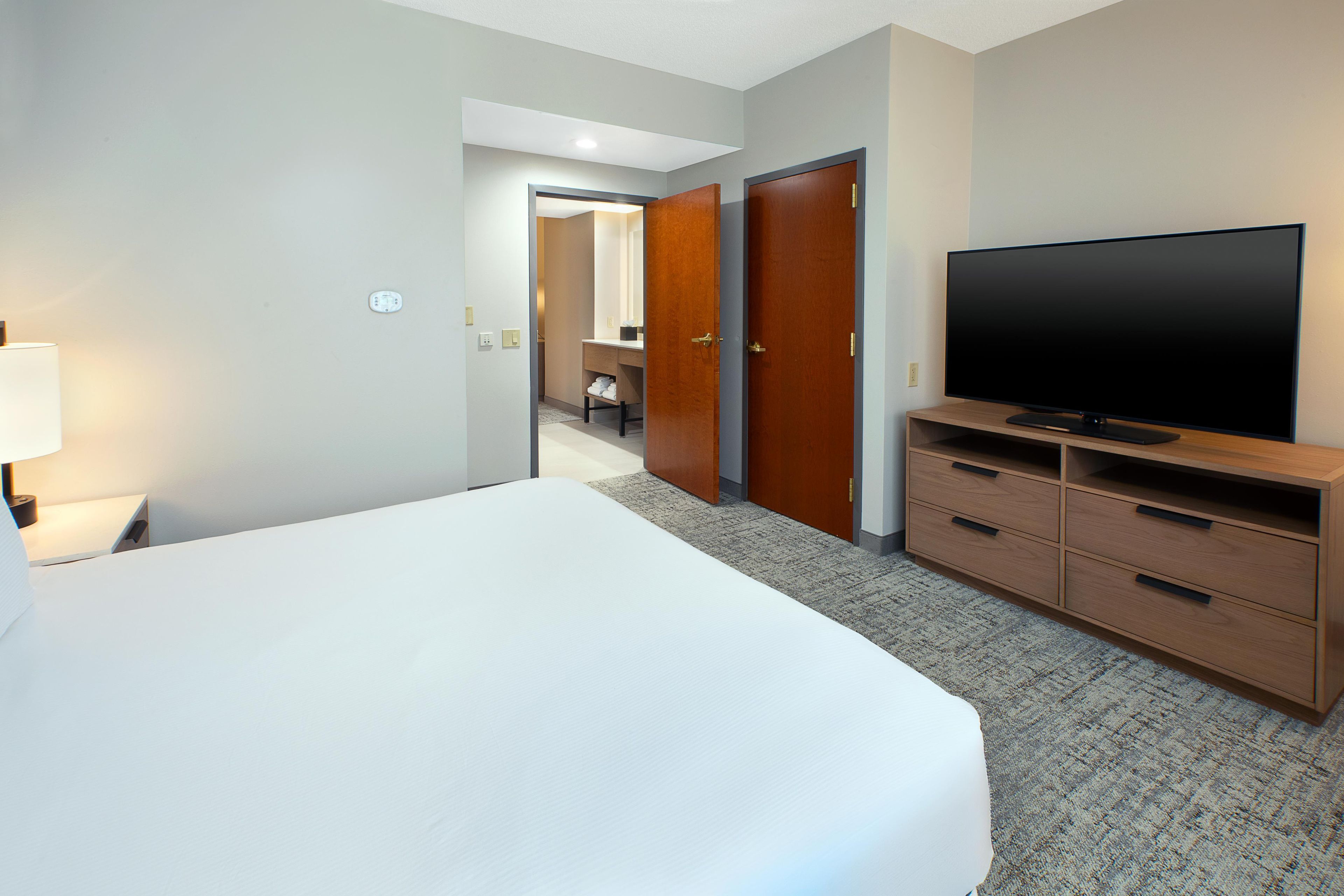 A hotel room with a large bed, a television on a wooden stand, and a bathroom visible through an open door.
