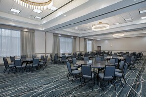 Un salón de conferencias con varias mesas y sillas, ventanas amplias con cortinas y suelo alfombrado.
