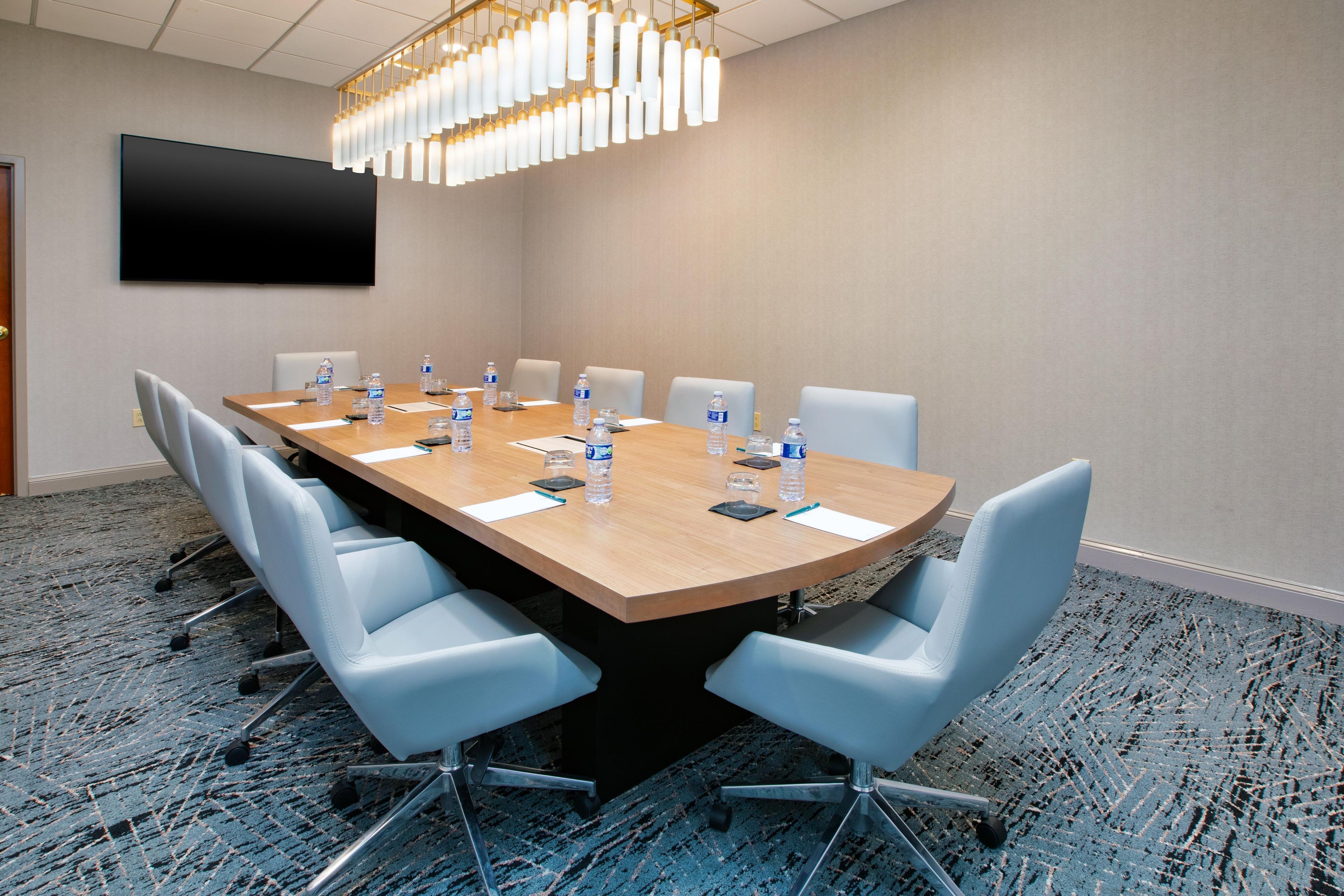 A conference room with a long table, chairs, water bottles, and a flat-screen TV on the wall.