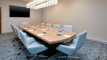 A conference room with a long table, chairs, water bottles, and a flat-screen TV on the wall.