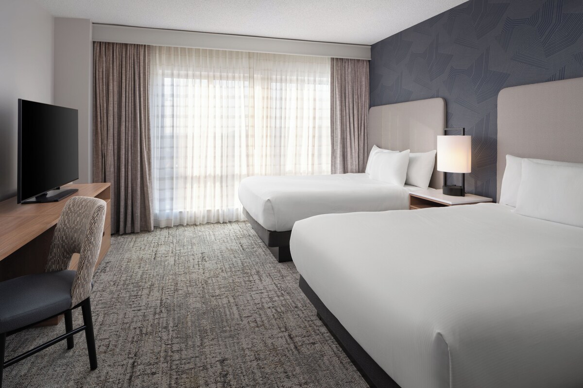 A hotel room with two beds, a desk with a TV, and a chair.