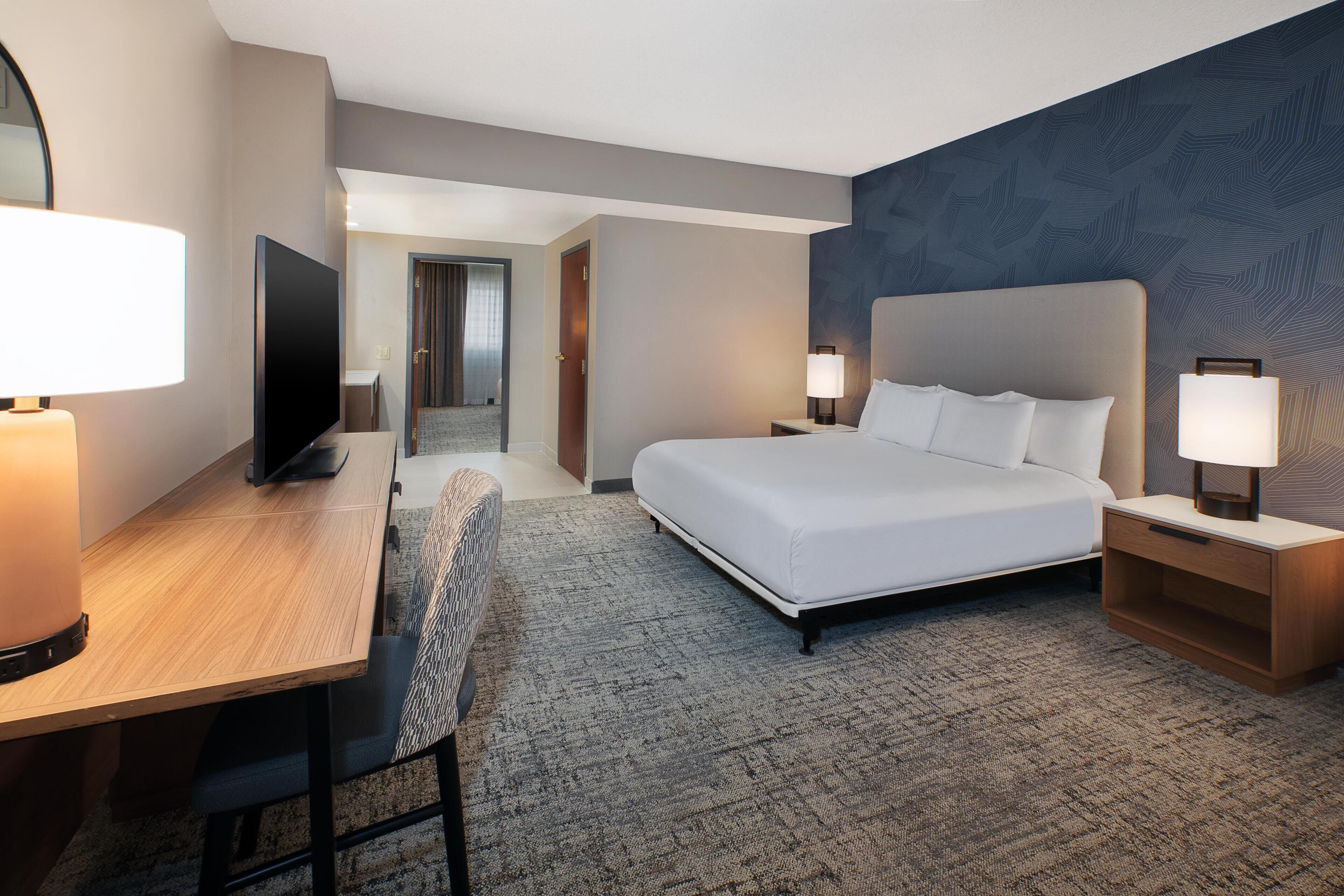 Una habitación de hotel con una cama, un escritorio, un televisor y una silla.