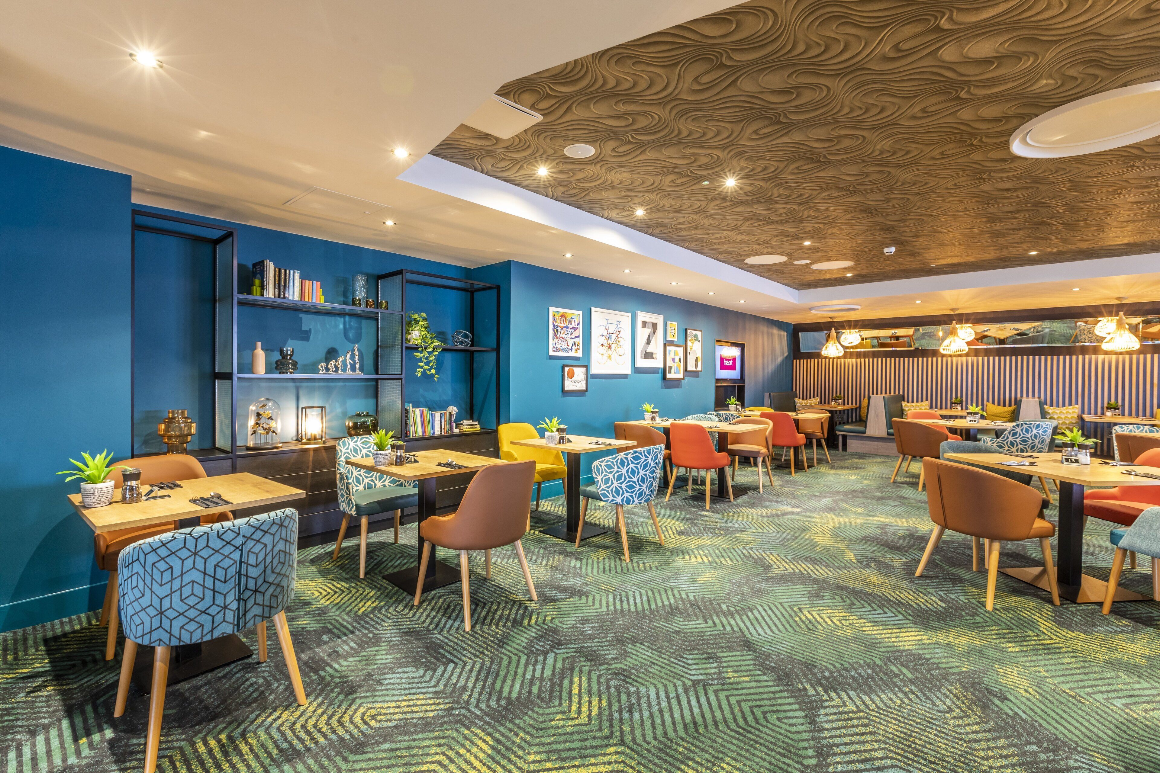 Un ristorante moderno con pareti blu, soffitto in legno e sedie colorate.