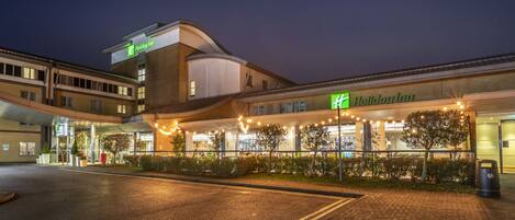 Un hôtel Holiday Inn au design moderne, doté d’une entrée couverte et d’un éclairage extérieur.