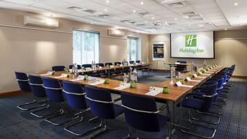 A conference room with a long table, blue chairs, name cards, and a projector screen displaying the Holiday Inn logo.